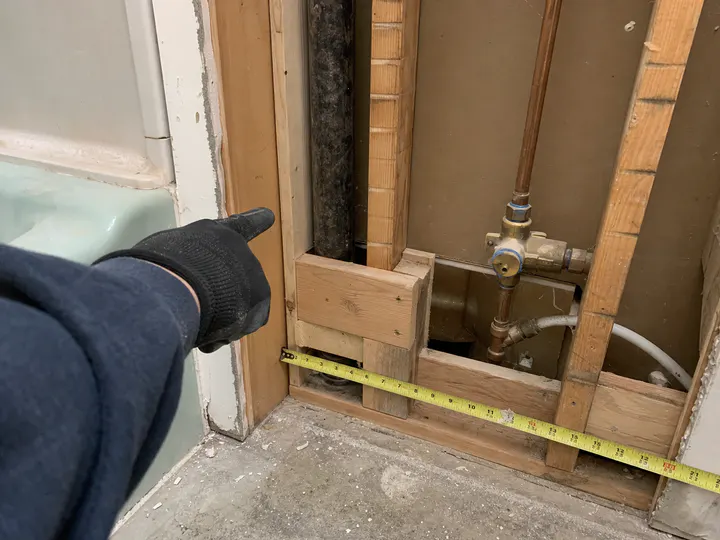 Open bathroom wall with a worker pointing to an inspection issue